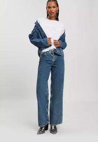 Jeansowa kurtka o luźnym kroju, zestawiona z białą koszulką i niebieskimi spodniami o szerokich nogawkach. Dodatkiem są srebrne buty na wysokim obcasie.