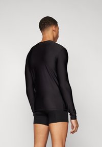 Camisetta nera a maniche lunghe realizzata in tessuto liscio e elasticizzato, con un semplice scollo rotondo e design aderente, abbinata a pantaloni corti neri.