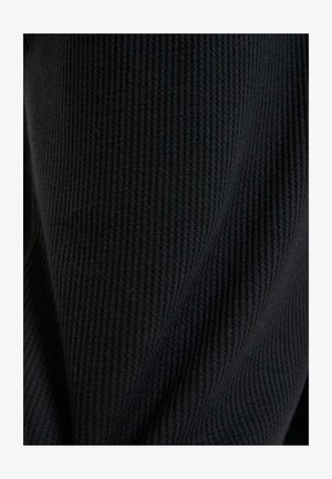 Gros plan sur un tissu noir à côtes, présentant une surface texturée avec des lignes verticales et une apparence douce et tissée.