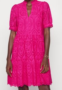 Rosa broderad klänning med lagerdesign, vågig fåll, korta puffärmar och en nyckelhålsöppning med blomstermönster.