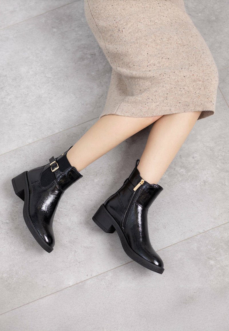 Zwarte gepatenteerde enkelboots met een chunky hak, voorzien van een zijrits, elastische accenten en een gladde, glanzende textuur.