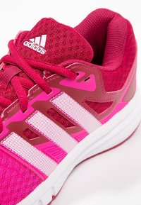 Scarpa sportiva Adidas con parte superiore in rete rosa, dettagli bianchi e suola ammortizzata. Il design include tre strisce distintive e fori di ventilazione.