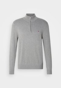 Maglione grigio con zip realizzato in tessuto a maglia, dotato di un colletto alto e maniche lunghe. Un piccolo logo sul petto aggiunge un tocco di dettaglio.
