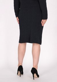 Dunkelblaues Strickkleid mit Zopfstrickmuster, figurbetontem Design, knielanger Saum, kombiniert mit schwarzen Stiletto-Absätzen. Strukturierte Stoffoberfläche.