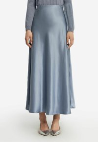 Jupe longue et fluide en satin bleu clair avec une taille haute. Texture lisse et silhouette en A, associée à des escarpins argentés à bout pointu.