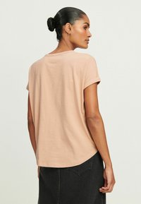 Lyserød kortærmet t-shirt med rund hals, afslappet pasform og oprullede ærmer, parret med en mørk denimnederdel.