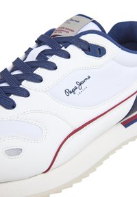 Adidași albi cu șireturi și accente bleumarin. Prezintă un design texturat, detalii cu logo pe lateral și o linie roșie pe talpă.
