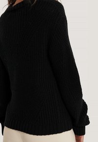 Czarny sweter z dzianiny o teksturowanym, prążkowanym wzorze, z luźnym krojem i oversized rękawami. Widoczne detale szwów na plecach.