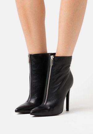 Sorte ankelstøvler i læder med spids snude, sølvfarvet lynlåssyning og stiletthæl. Glat tekstur med bløde folder ved anklen.