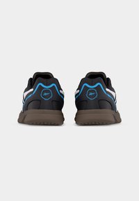 Ζεύγος μαύρα αθλητικά παπούτσια με μπλε και λευκές λεπτομέρειες, ορατά από πίσω, με καφέ σόλες και στρογγυλό λογότυπο στις φτέρνες.