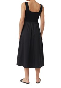 Schwarzes Maxikleid mit quadratischem Ausschnitt, breiten Trägern und gerafftem Taillenbund, aus weichem Stoff, der bis zur Mitte der Waden reicht.