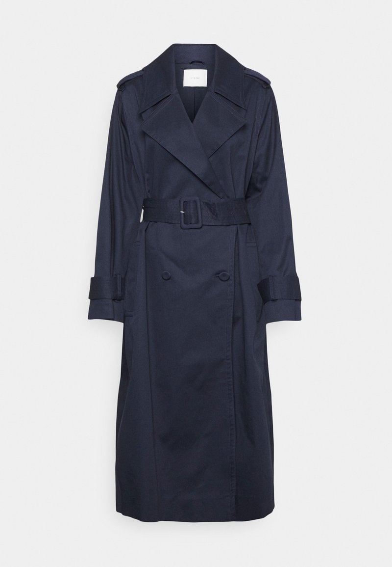 Trench-coat bleu marine foncé avec larges revers, boutons croisés, ceinture à la taille et sangles aux poignets, suspendu sur un fond blanc.