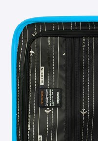 Modrý obal na zip s vnitřní stranou v černé barvě, pokrytý bílými vzory letadel a textem. Obsahuje síťovanou kapsu a textilní značkovou etiketu.