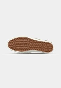 Vit sneakersula med ett texturerat brunt gummiträd och en liten läpp; har en slät, flexibel ovandel fäst med metallkomponenter.
