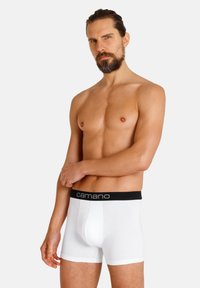 Weiße Baumwoll-Boxershorts mit einem schwarzen elastischen Bund, der das Logo "camano" trägt; glatte Textur, figurbetontes Design.