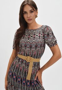 Sukienka w wzory z czarnym tłem, zdobiona wielokolorowymi, pióropodobnymi wzorami. Krótkie bufiaste rękawy oraz beżowy pasek z okrągłą klamrą.
