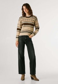 Gebreid sweater in beige met bruine en blauwe ruitpatronen, gecombineerd met donkere brede jeans en bruine haklaarzen.