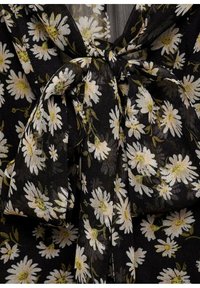 Svart tyg med blommönster som har vita tusenskönor och gröna stjälkar. En knytband detalj vid halsringningen ger textur.