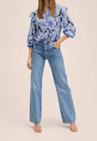 Chemise à boutons à fleurs avec manches à volants en bleu et noir, associée à un jean taille haute à jambes larges bleu clair et des sandales rose pâle.