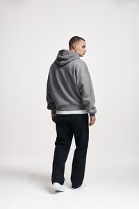 Young man facing away, wearing a grey hoodie, white shirt, black jeans, and white sneakers against a plain white background.