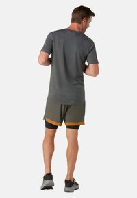 Camiseta atlética gris combinada con shorts oliva que presentan una franja de acento marrón. La tela parece ligera; el ajuste es holgado.