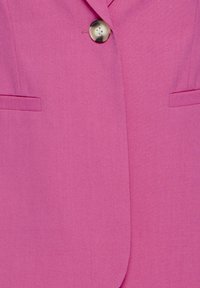 Veste rose vif avec un grand bouton en écaille de tortue et deux poches horizontales fendues à l'avant.