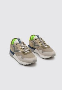 Baskets rétro beiges et gris avec des matériaux en daim et en maille, des accents réfléchissants, une doublure néon verte et une semelle en caoutchouc blanche.