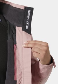 Roze waterdichte jas met een zwarte fleece voering en een ritszak. Voorzien van een merklabel op de kraag en klittenbandsluiting bij de manchetten.