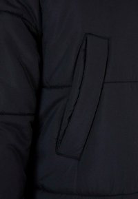 Crni pufast jakna sa dijagonalnim šavom, s skrivenim bočnim džepom i glatkom, teksturiranom tkaninom. Mekan, izoliran materijal.