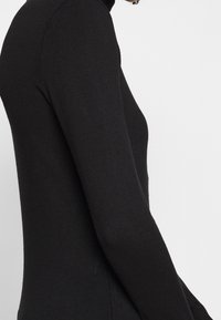 Czarny sweter z golfem o dopasowanym kroju, wykonany z gładkiej dzianiny, z długimi rękawami i wysokim kołnierzem.