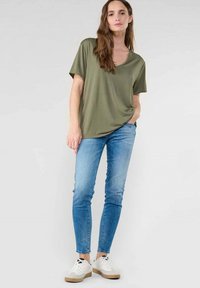 Top corto de color verde oliva con escote redondeado, combinado con jeans ajustados de color azul claro y zapatillas blancas con suela beige.