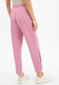 Rosa Jogginghosen aus weichem Stoff mit lockerer Passform, elastischem Bund und seitlichen Schlitzen an den Knöcheln. Kombiniert mit weißen Sneakern.