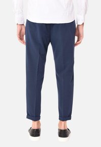 Pantaloni blu navy con una vestibilità aderente, con risvolti e una texture liscia, abbinati a sneaker nere e una camicia bianca.