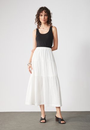 Top negro sin mangas combinado con una larga falda blanca de volantes con tela texturizada. Completado con mule negros de tacón.
