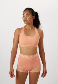 Peach sports bra and shorts set made of stretchy, smooth fabric. Features logo accents and mesh panels for breathability.