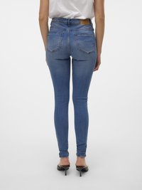 Høyt midjebutikk blå jeans med en jevn tekstur, som har to baklommer og et brunt lærmerke i livet. Tettsittende silhuett.