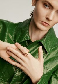 Anillo de oro con un diseño en forma de estrella que presenta piedras preciosas moradas. Modelo vistiendo una chaqueta verde brillante, mostrando el anillo en la mano izquierda.