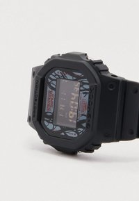 Digitaalne käekell musta plastist korpuse ja rihmaga. Kellal on mustriline sinine sihverplaat puude ja "Stranger Things" kaubamärgiga.