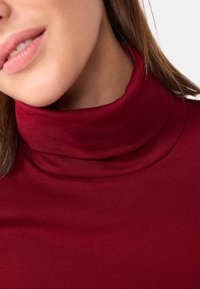 Maglietta a collo alto bordeaux con texture a coste. Primo piano che mostra il tessuto morbido e il design con colletto alto.
