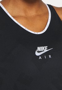 Svart Nike linne med en kontrasterande vit halsringning med "AIR"-mönster och en framträdande silverfärgad Nike-logga på bröstet. Slät textur.