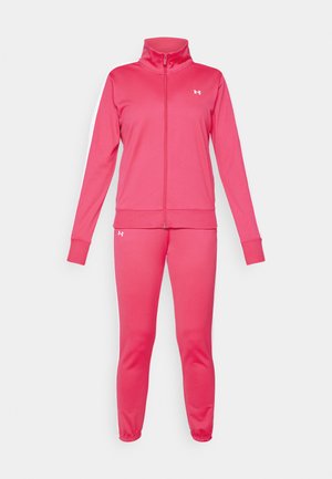 Roze trainingspak met een ritssluiting jacket en bijpassende broek. Heeft een hoge kraag, geribbelde manchetten en witte zijstrepen. Gemaakt van zacht, flexibel materiaal.