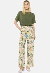 Olive green short-sleeve top paired with wide-leg beige trousers featuring a floral pattern in blue, green, and pink. Light purple heeled shoes.