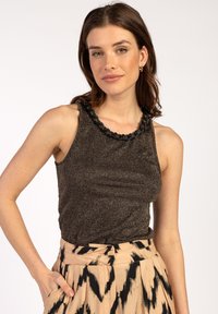 Mouwloze tanktop in donkerbrons met een gestructureerde afwerking en een zwarte gevlochten halslijn. In combinatie met een patroonrok met zwarte strepen.