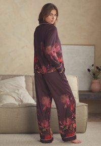 Lila virágos pizsamaszett selymes anyaggal. Nagy, rózsaszín és piros virágmintákkal, kontrasztos fehér szegéllyel és kényelmes, laza szabással.