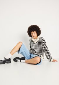 Maglione a righe in bianco e nero con colletto crema, abbinato a pantaloni shorts in denim azzurro chiaro. La modella indossa scarpe Mary Jane nere e calzini bianchi.