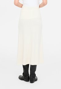 Falda larga de punto color crema con cintura acanalada y textura sutil, combinada con botas negras hasta la rodilla con un detalle de hebilla.