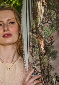 Leichte, gemusterte Schals mit botanischen Motiven und Vögeln, mit einem fransigen Rand. Das Model trägt ein strukturiertes Oberteil und zarte goldene Schmuckstücke.