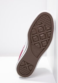 Semelle en caoutchouc marron d'une sneaker bordeaux avec des garnitures blanches, présentant un motif texturé et un logo de marque.