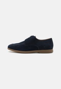 Pantofi eleganți din suede albastru marin, cu un finisaj neted, bot rotund și talpă din cauciuc bej. Dispune de cinci perechi de găuri pentru șireturi.