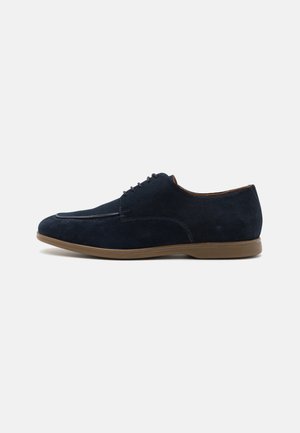 Scarpe eleganti in camoscio blu navy con finitura liscia, punta arrotondata e suola in gomma color beige. Presentano cinque paia di occhielli per la lucidatura.